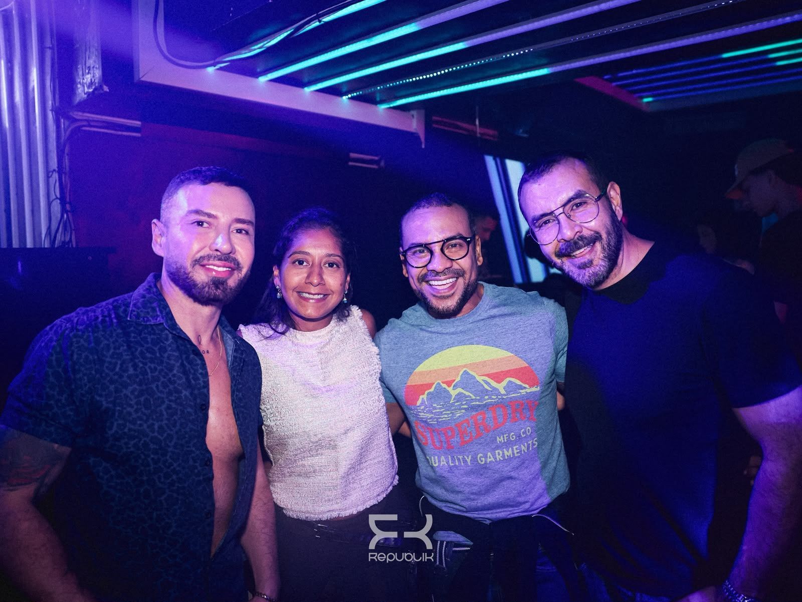 Cuatro personas sonrientes posando juntas en un club iluminado con luces de neón moradas y azules
