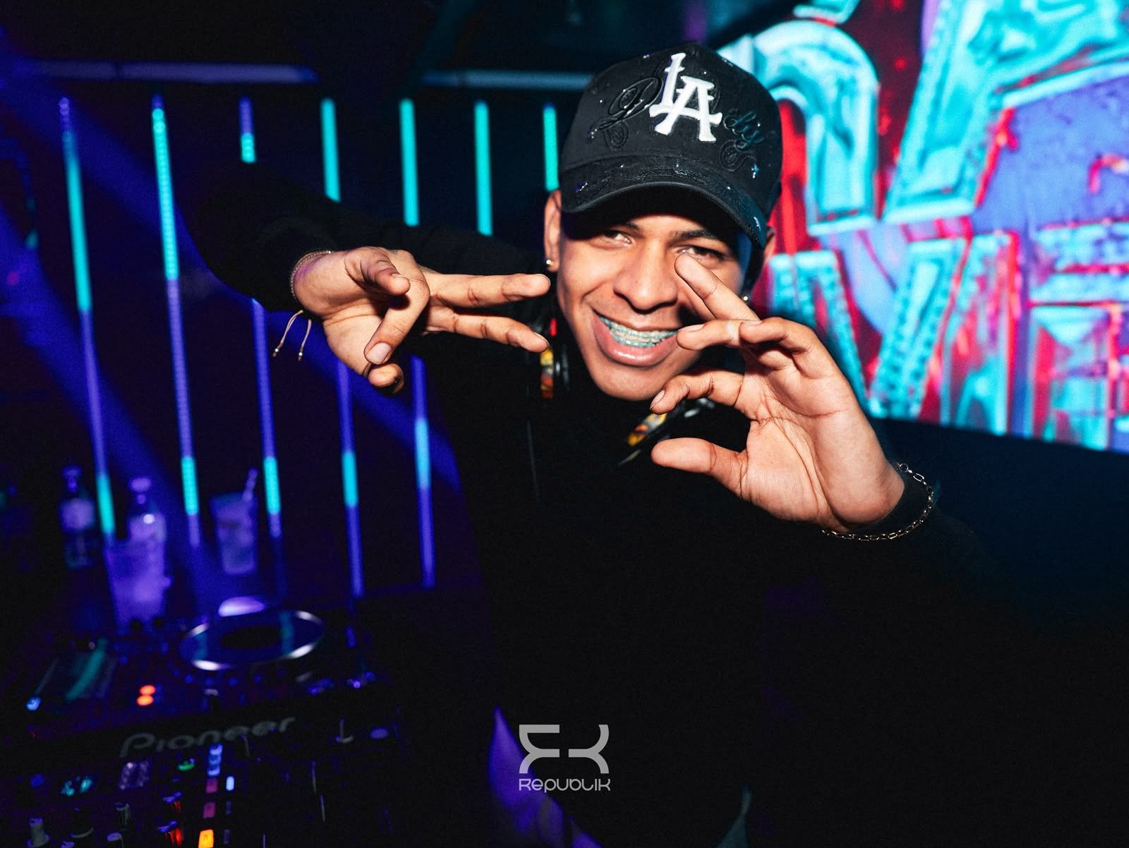 Persona sonriendo y haciendo gestos con las manos en una discoteca iluminada con luces de neón azules y rosas