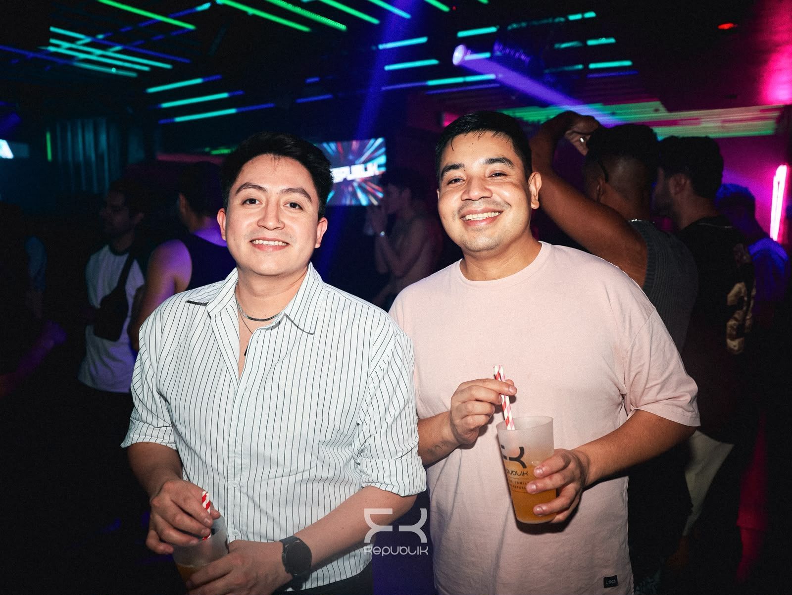 Dos personas sonríen y sostienen bebidas en una fiesta en una discoteca llena de color