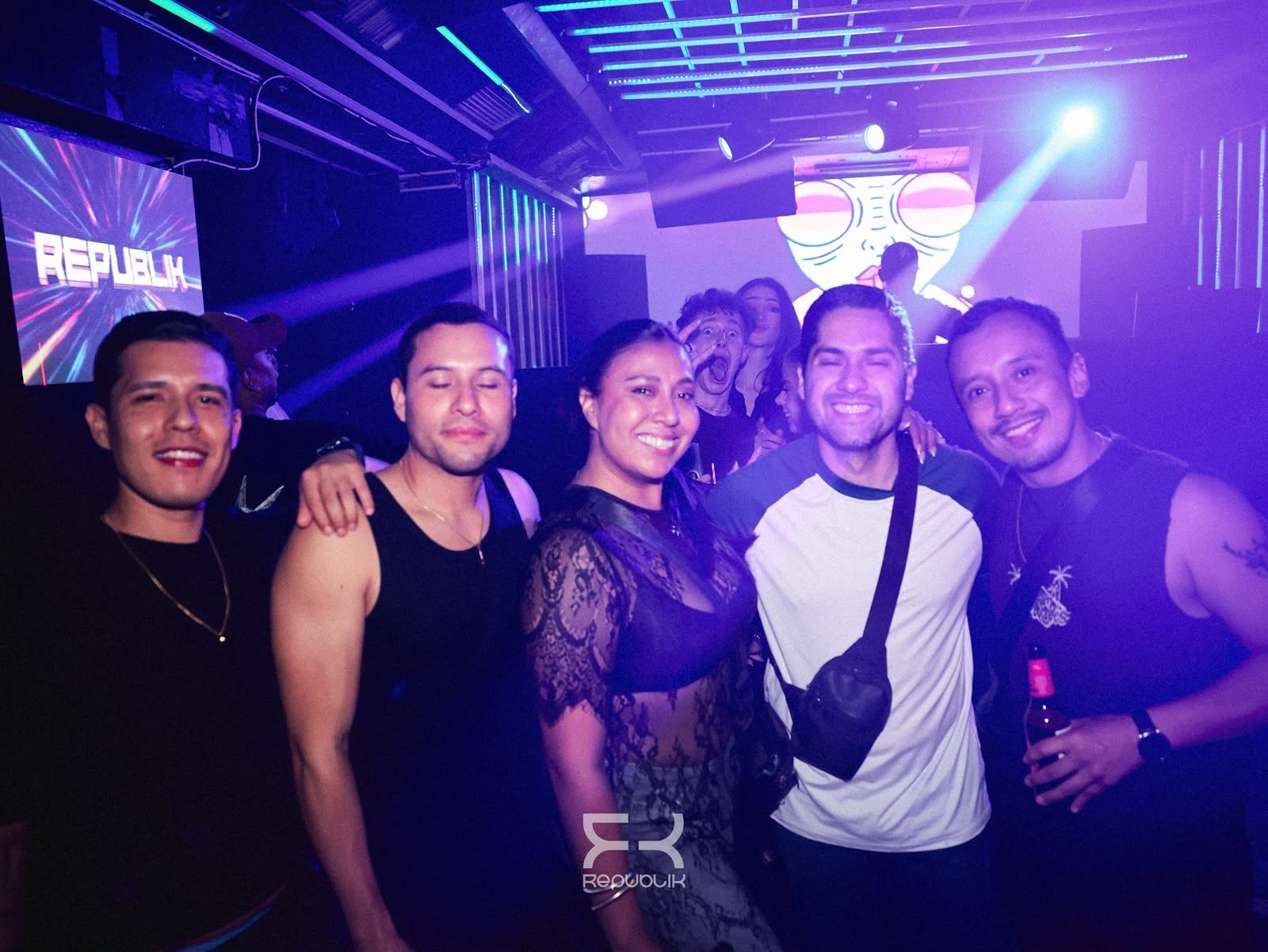 Cinco amigos sonrientes posando en una discoteca iluminada con luces de neón moradas