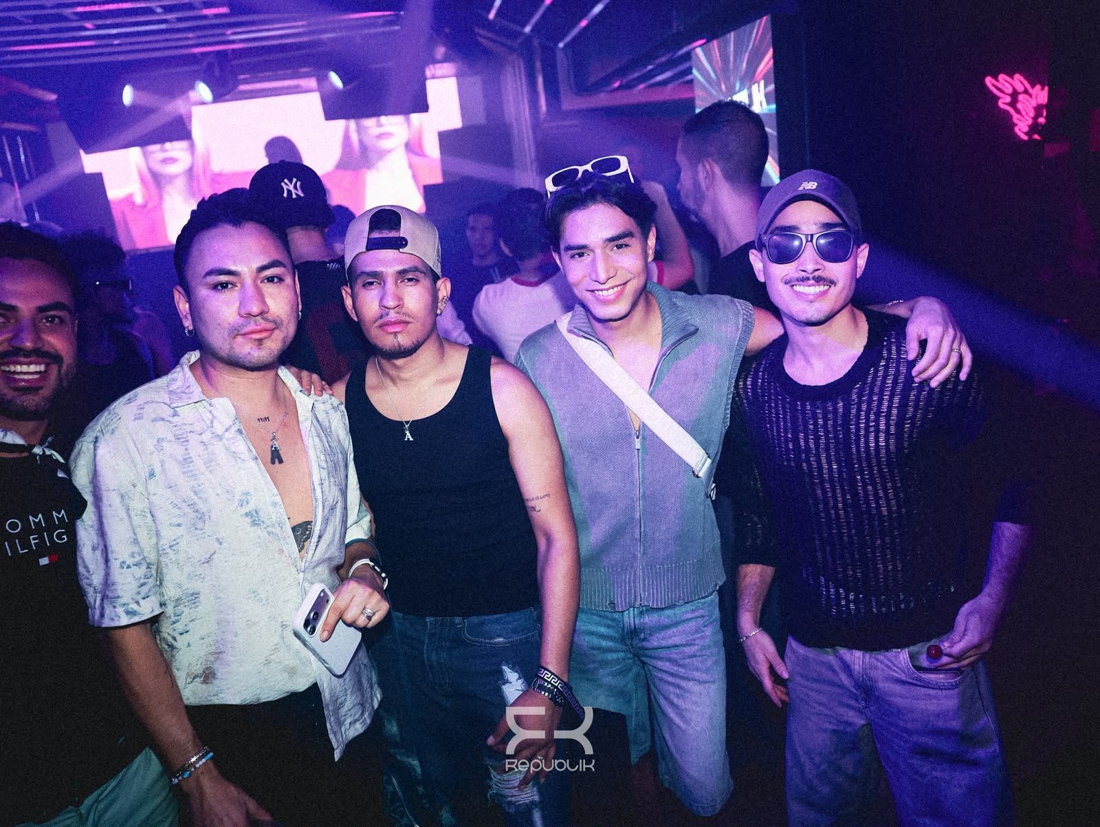 Cuatro amigos posando juntos en una discoteca, con luces moradas y bebidas en la mano.