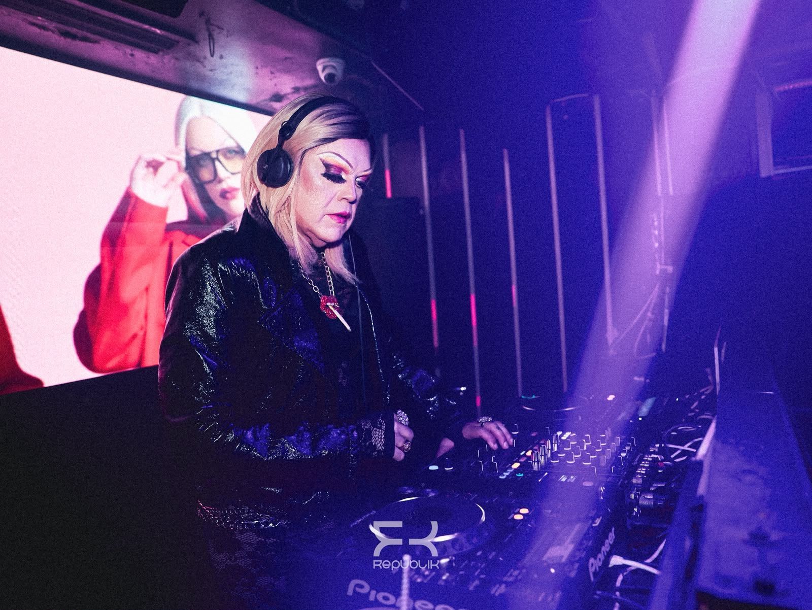 DJ actuando en una discoteca con luces moradas, con auriculares y mezclando música en la mesa de mezclas