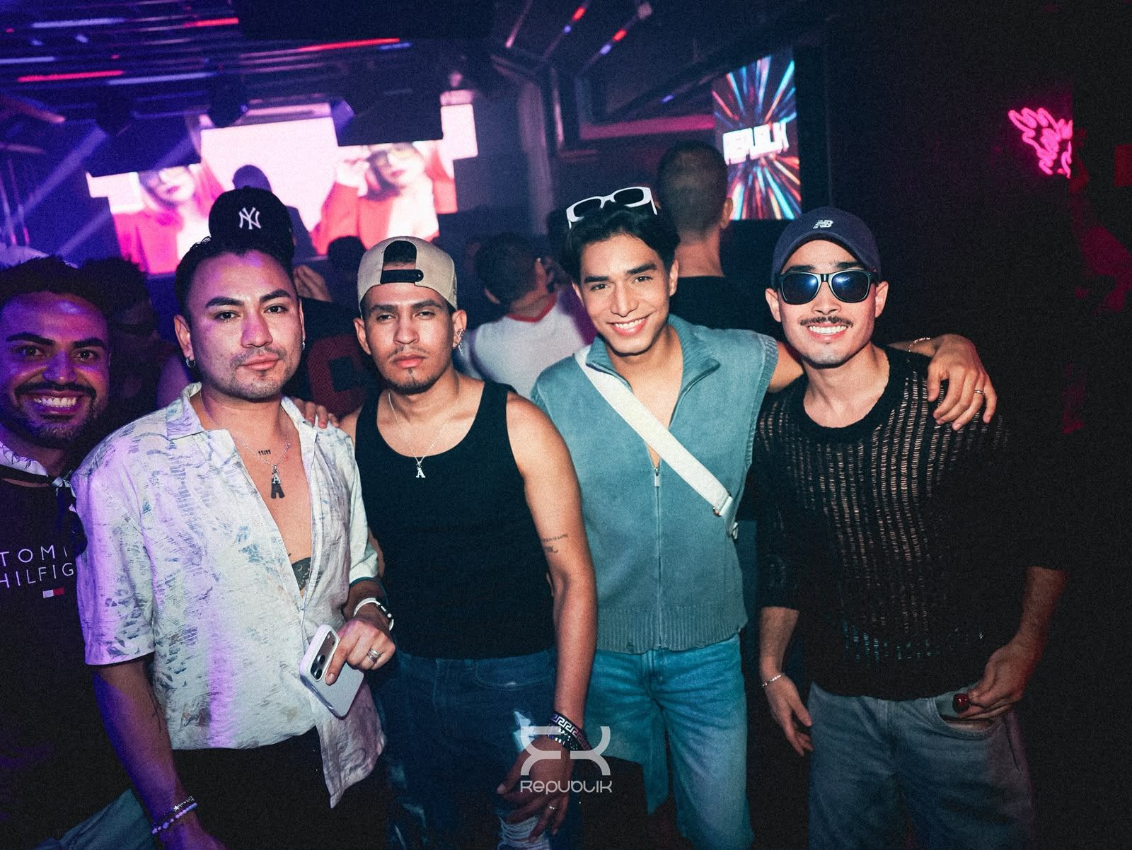 Cinco amigos posando en una discoteca con poca luz, luces de neón de colores y una cabina de DJ al fondo