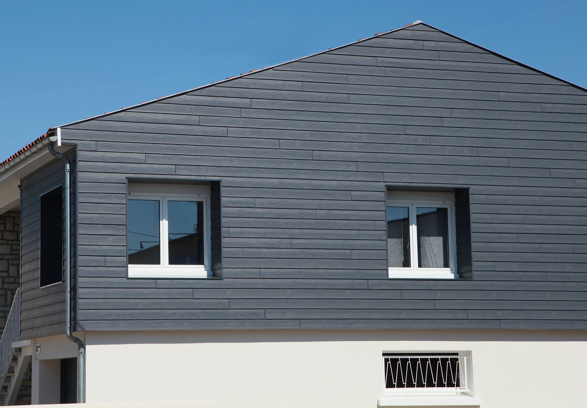 Maison avec deux fenêtres et un bardage noir.
