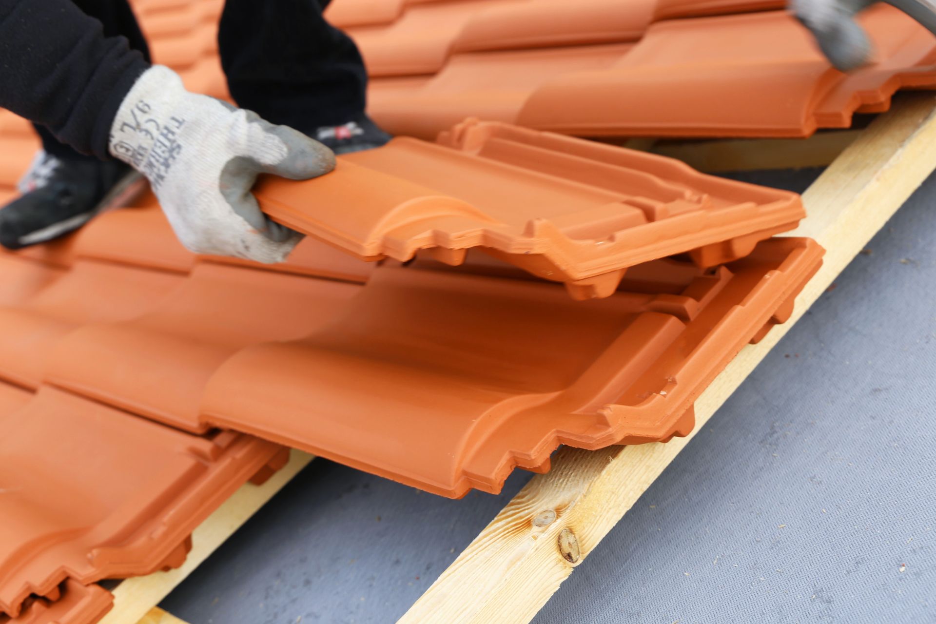 Ouvrier empilant des tuiles orange sur une palette en bois.