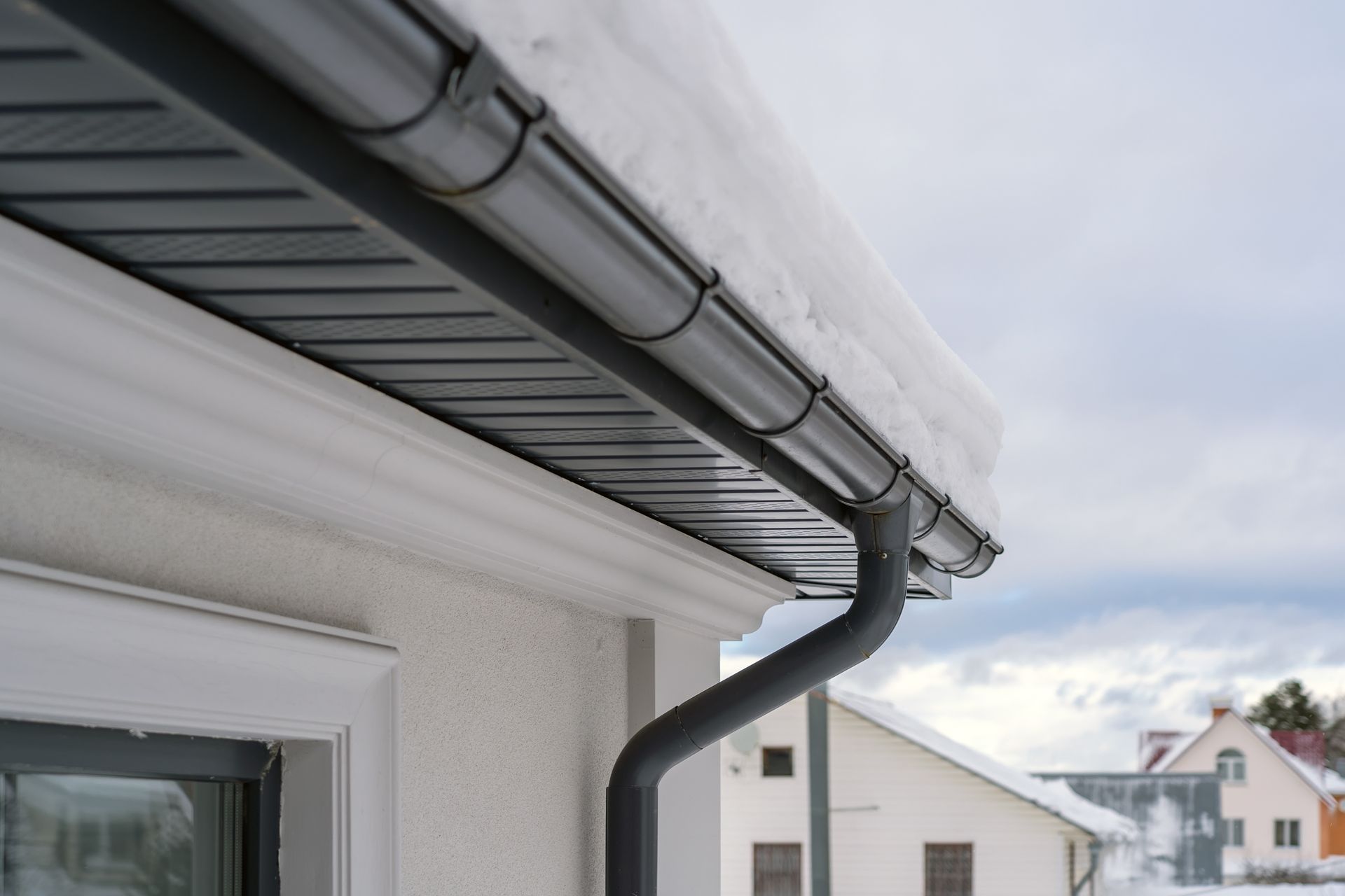 Avant-toit d'une maison avec gouttière et descente pluviale noires.