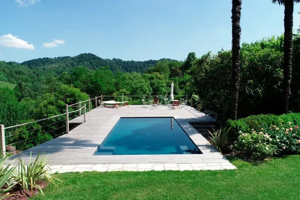 Una grande piscina è circondata da una vegetazione lussureggiante e da un ponte in legno