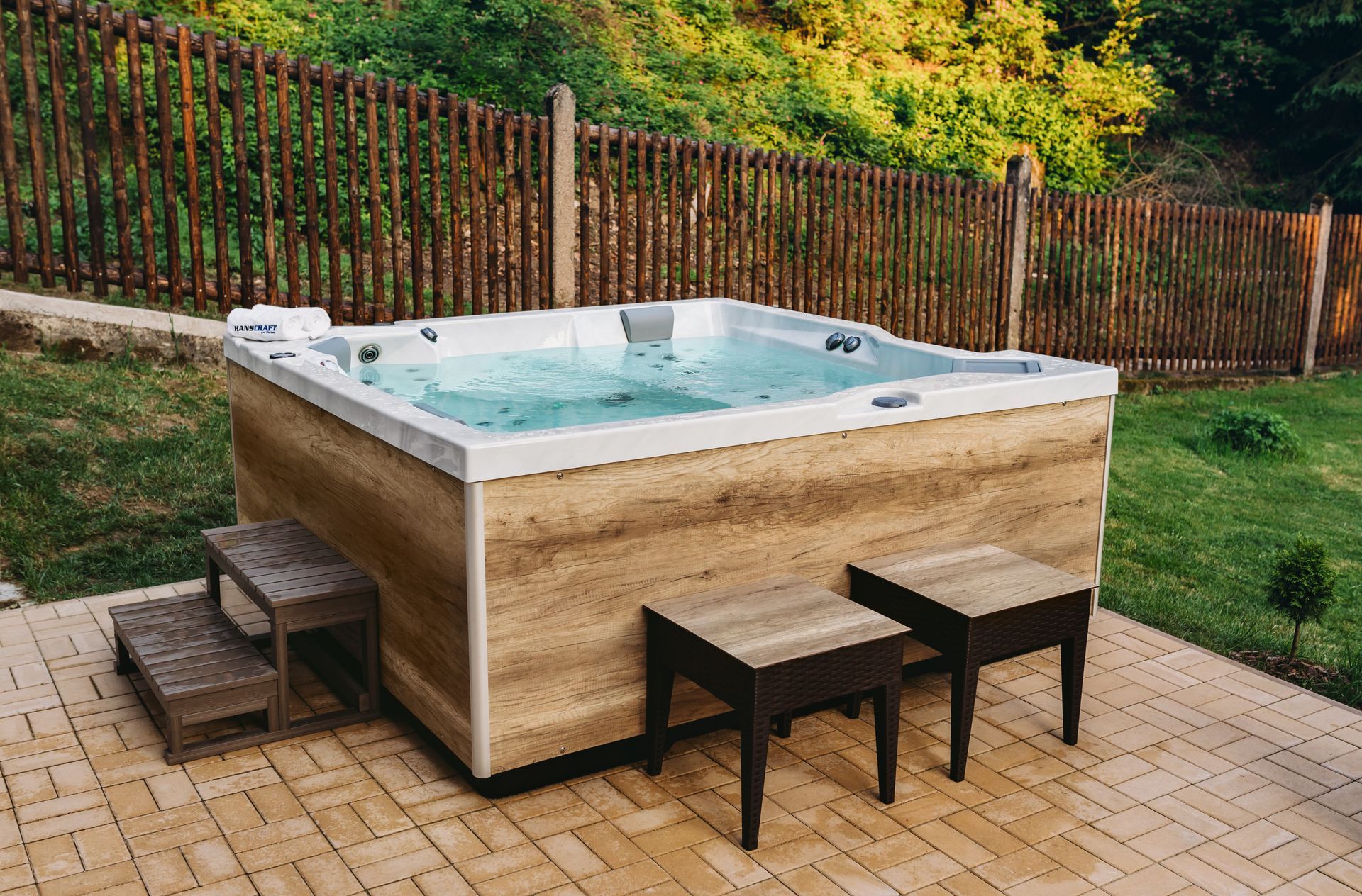 Una vasca idromassaggio è posizionata su un patio in mattoni accanto a una staccionata in legno.