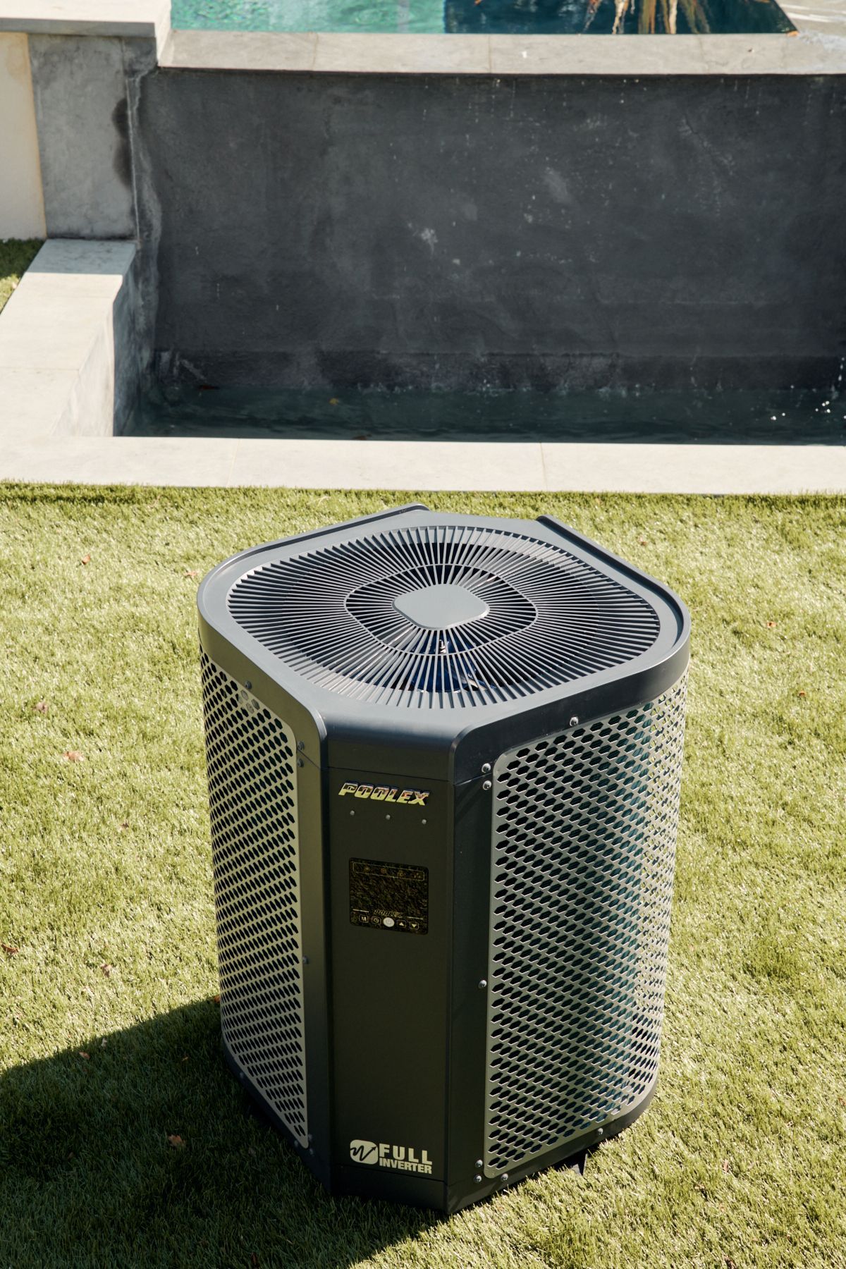 Un condizionatore nero è appoggiato su un rigoglioso prato verde accanto a una piscina.