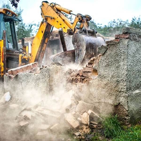 Una excavadora está demoliendo un edificio en un campo.