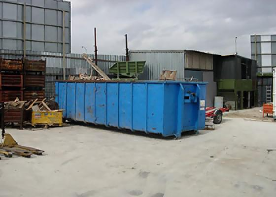 Un gran contenedor de basura azul está estacionado frente a un edificio.