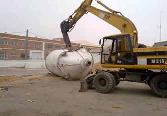 Una excavadora amarilla y negra está cargando un tanque grande en un camión.