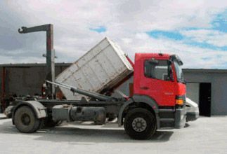 Un camión volquete rojo con un contenedor blanco en la parte trasera está estacionado frente a un edificio.