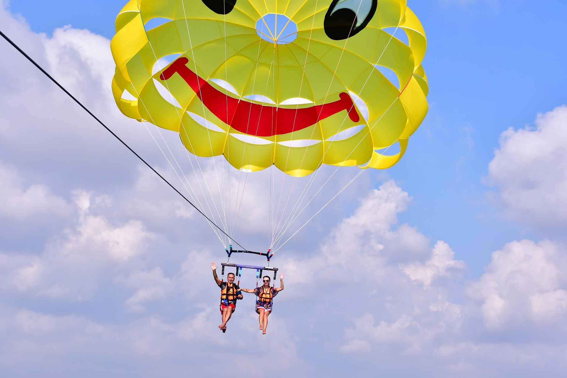 Deux personnes font du parachute ascensionnel sous un parachute jaune à motif de smiley au-dessus de l'océan sous un ciel nuageux.