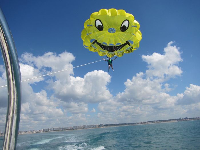 Parachute ascensionnel au-dessus de l'océan bleu, avec un parachute coloré et un  bateau au premier plan.