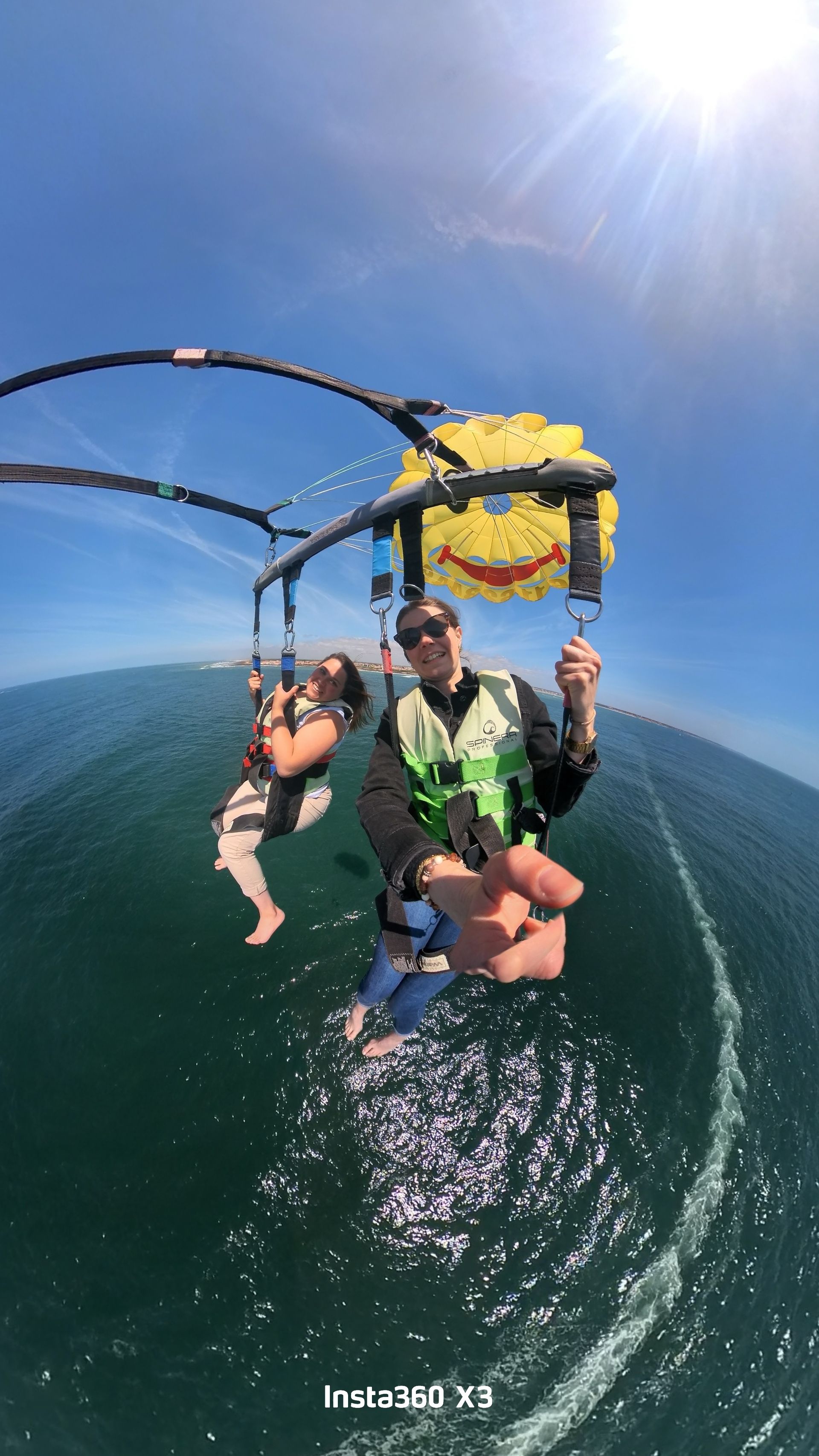 Deux personnes font du parachute ascensionnel au-dessus de l'océan sous un ciel d'un bleu éclatant, attachées à un parachute jaune.