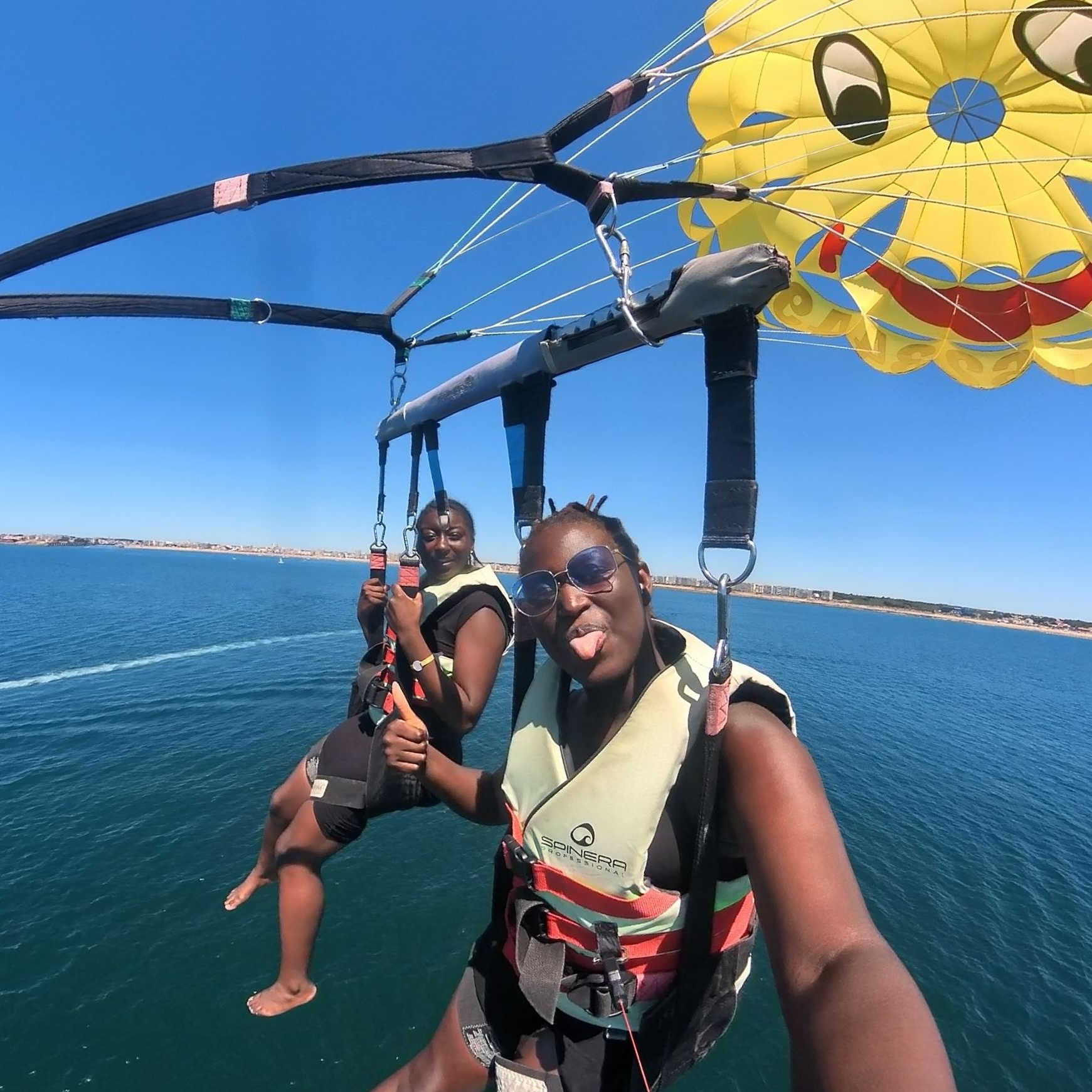Deux personnes font du parachute ascensionnel au-dessus d'une eau bleue, sous un auvent jaune vif, par une journée ensoleillée.