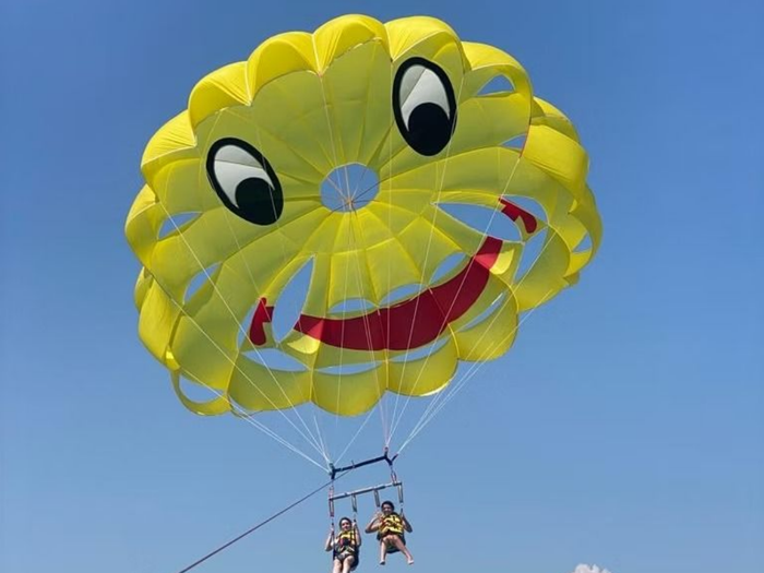 Parachute jaune à tête souriante transportant deux personnes sur fond de ciel bleu