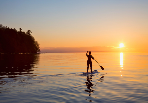 Person paddleboarding on calm water at sunset; orange sky, silhouette in the florida keys