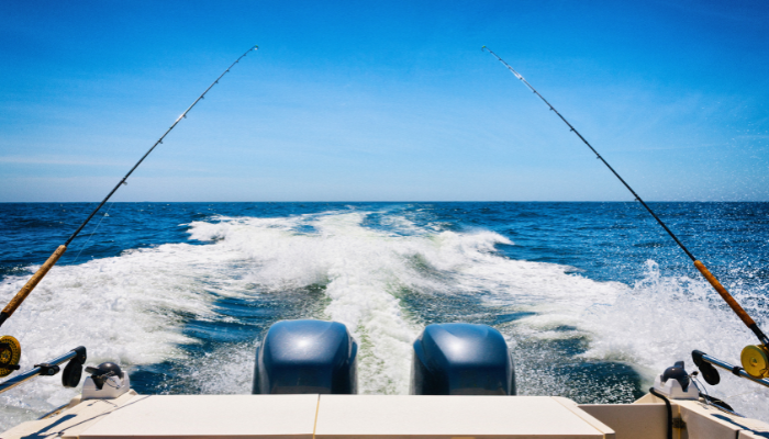 Fishing boat on the ocean, two fishing rods, two motors, blue water and sky.