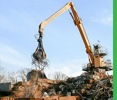 Une grosse excavatrice jaune soulève de la ferraille à l'aide d'une pince en forme de griffe dans un centre de recyclage.