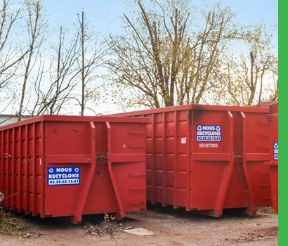 Deux grands conteneurs rouges à ordures à l'extérieur, avec des étiquettes de recyclage, sous un ciel bleu.