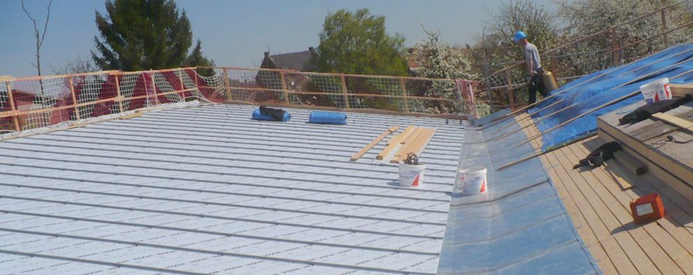 Toiture en construction avec des ouvriers, sous-couche bleue et rambardes de sécurité rouges sous un soleil éclatant