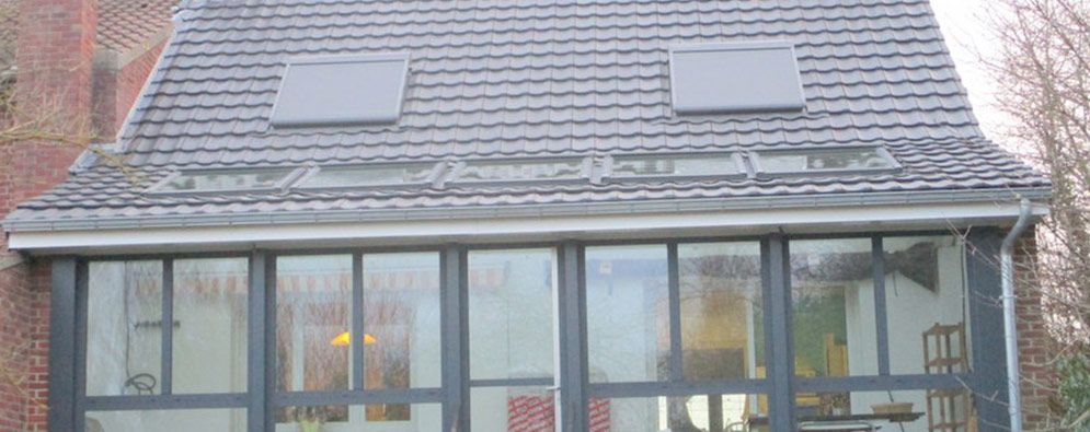 Toit en pente enneigé avec deux puits de lumière au-dessus d'une véranda vitrée