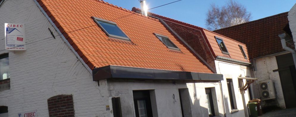 Maison blanche au toit de tuiles orange et aux puits de lumière, située dans une rue résidentielle ensoleillée.