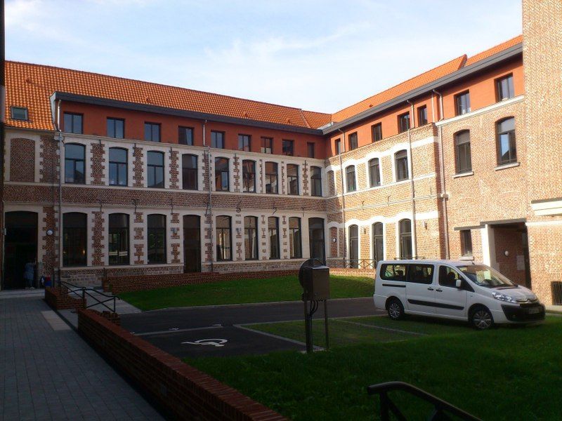 Cour intérieure d'un bâtiment en briques rouges aux fenêtres à encadrement blanc, pelouse verte et camionnette blanche garée à proximité.