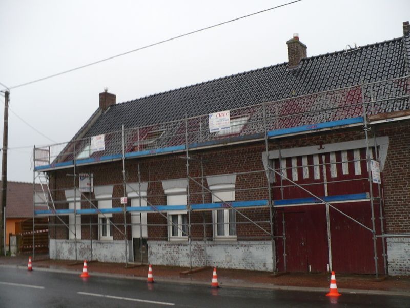 Échafaudages autour d'une maison en briques avec une porte de garage rouge et des cônes de signalisation orange sur une rue mouillée