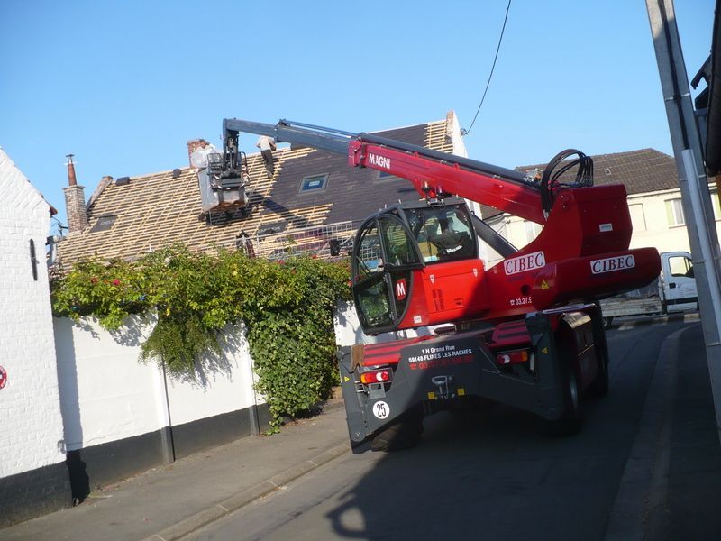 Camion-grue rouge soulevant des débris d'un toit endommagé dans une rue résidentielle
