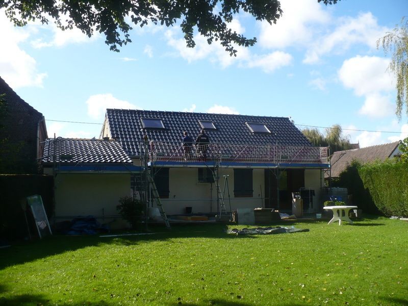 Jardin avec maison, pelouse verte, mobilier de terrasse et panneaux solaires sous un ciel bleu