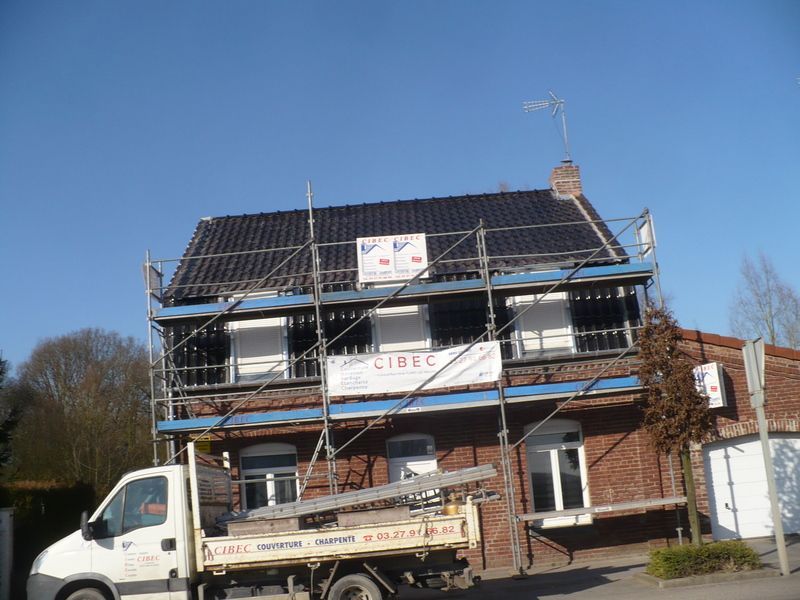 Maison en rénovation avec des échafaudages et un camion de chantier blanc devant, sous un ciel bleu clair.