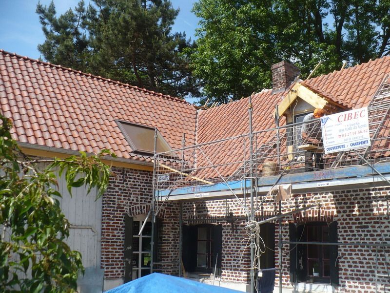 Cour intérieure avec bâtiments en briques et toits de tuiles rouges en cours de rénovation, recouverte d'échafaudages et de bâches.