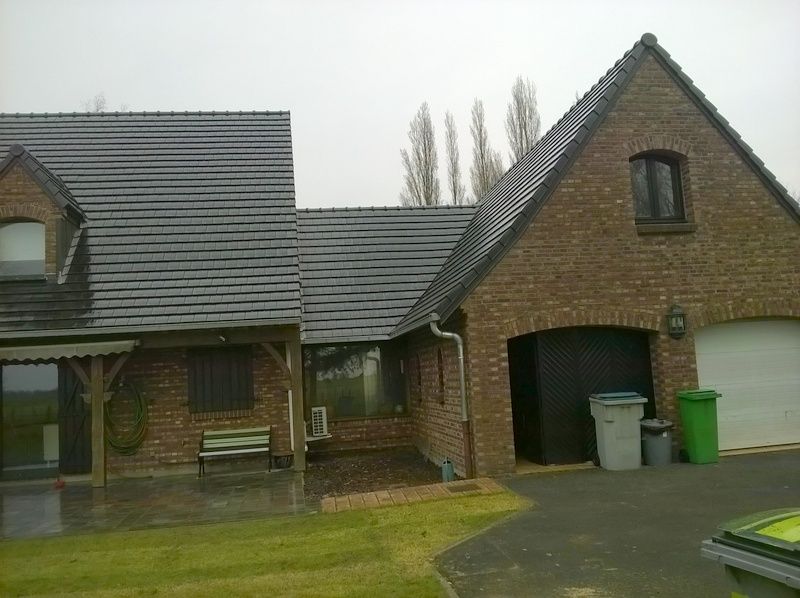 Maison en briques avec toit de tuiles foncées, allée et deux poubelles dans la cour avant