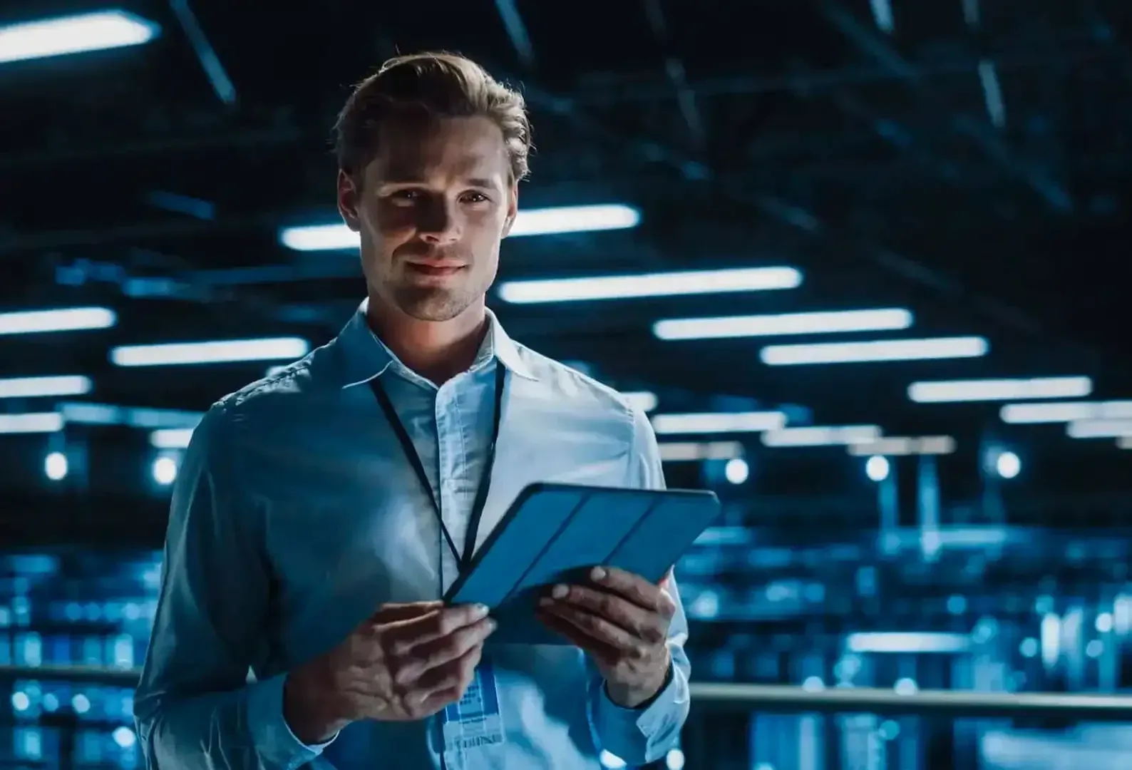 Una persona con una camisa azul claro sostiene una tableta en una sala de servidores de alta tecnología.