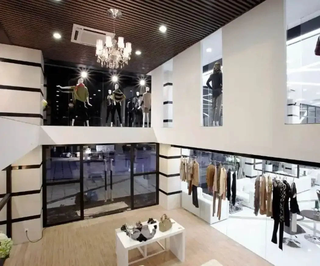 Una tienda de ropa de dos plantas con techos altos, lámpara de araña, escaparates.