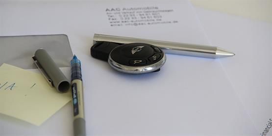 Ein Autoschlüssel liegt auf einem Stück Papier neben einem Stift und einem Haftnotizzettel.