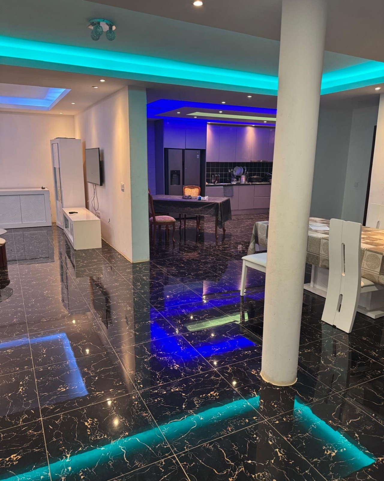 Intérieur moderne et spacieux avec sols en marbre noir, éclairage encastré et vue sur la cuisine.