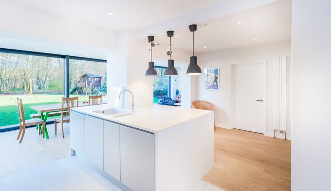 Cuisine blanche moderne avec îlot central, suspensions lumineuses et grande fenêtre donnant sur une cour.