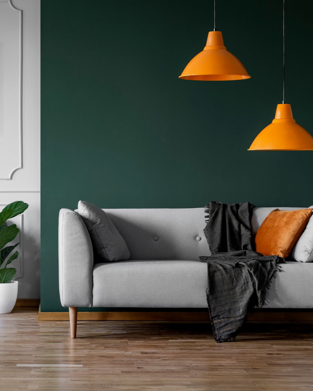 Canapé gris contre un mur vert foncé, deux suspensions orange, parquet.