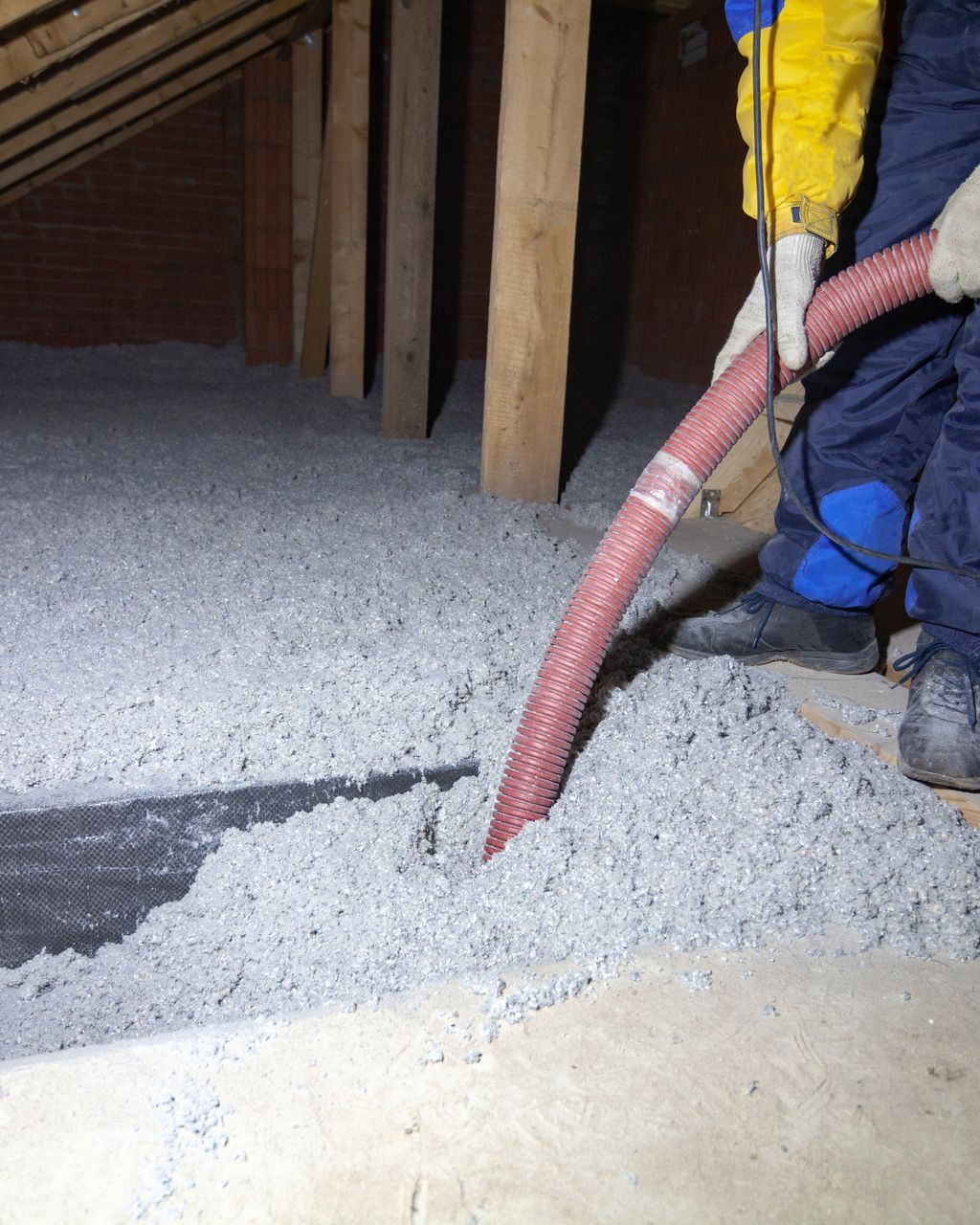 Une personne pulvérise de l'isolant cellulosique dans le plancher du grenier à l'aide d'un tuyau d'arrosage.