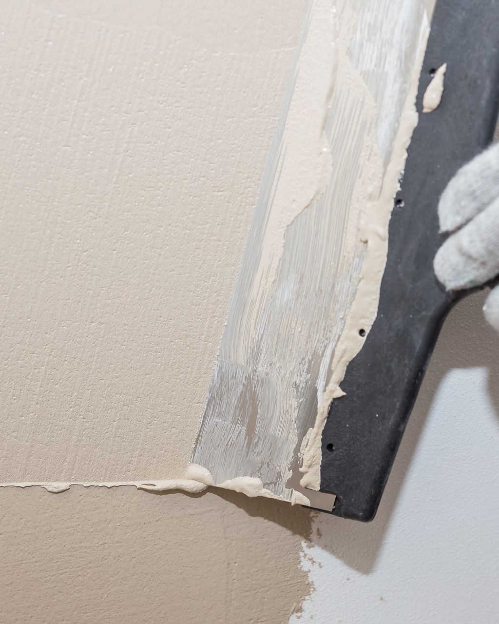 Une personne portant un gant blanc utilise une truelle pour appliquer de l'enduit à plaques de plâtre sur un mur.