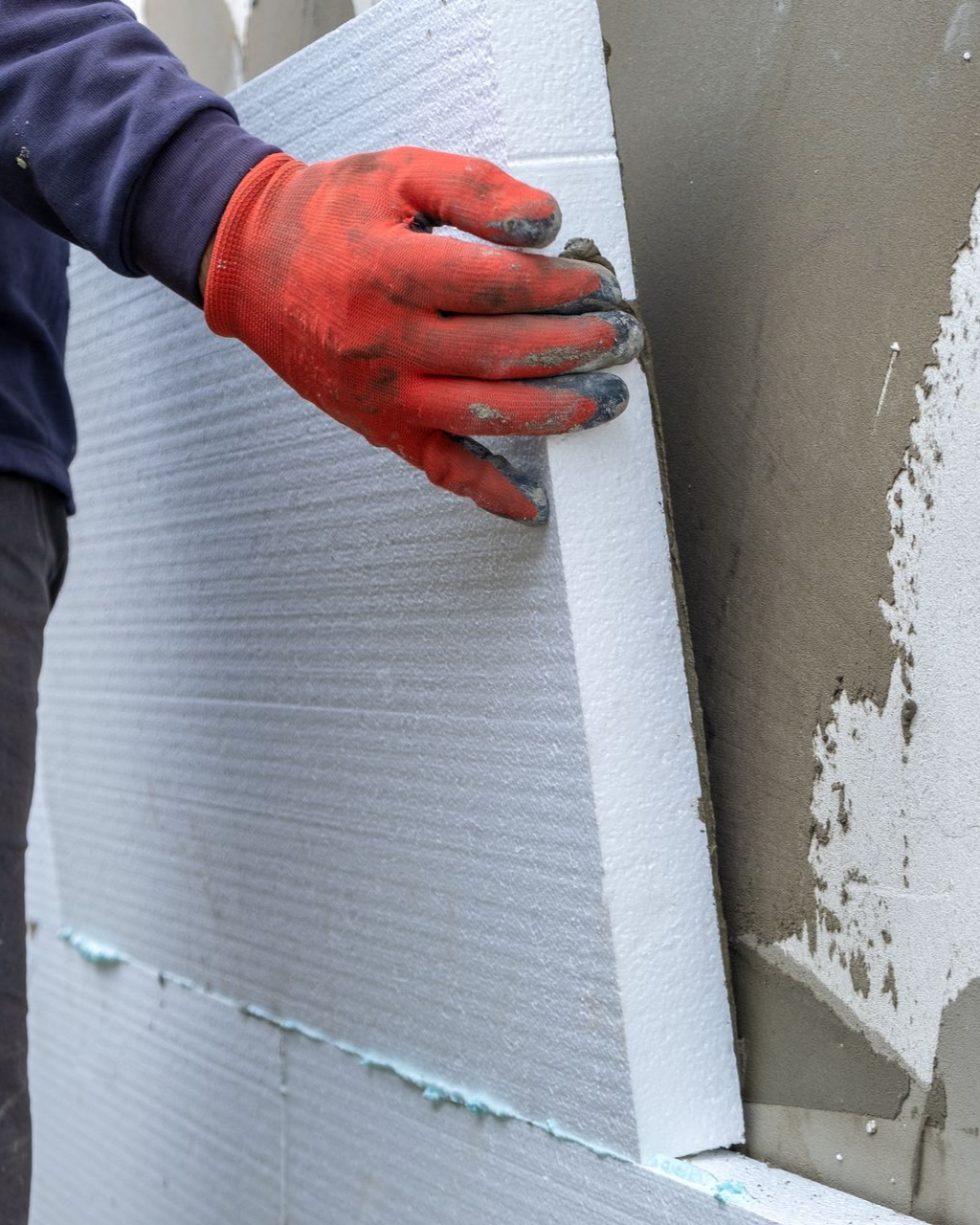 Une personne portant des gants rouges installe un panneau isolant sur un mur.
