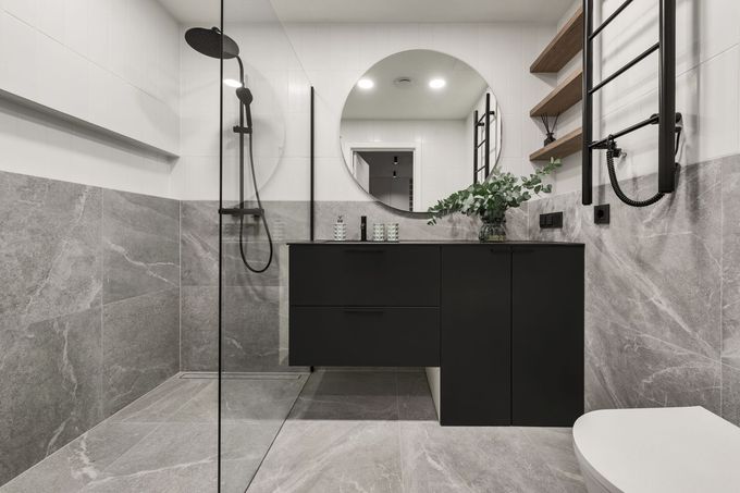Salle de bains moderne avec carrelage gris et blanc, meuble sous lavabo noir et douche à l'italienne.