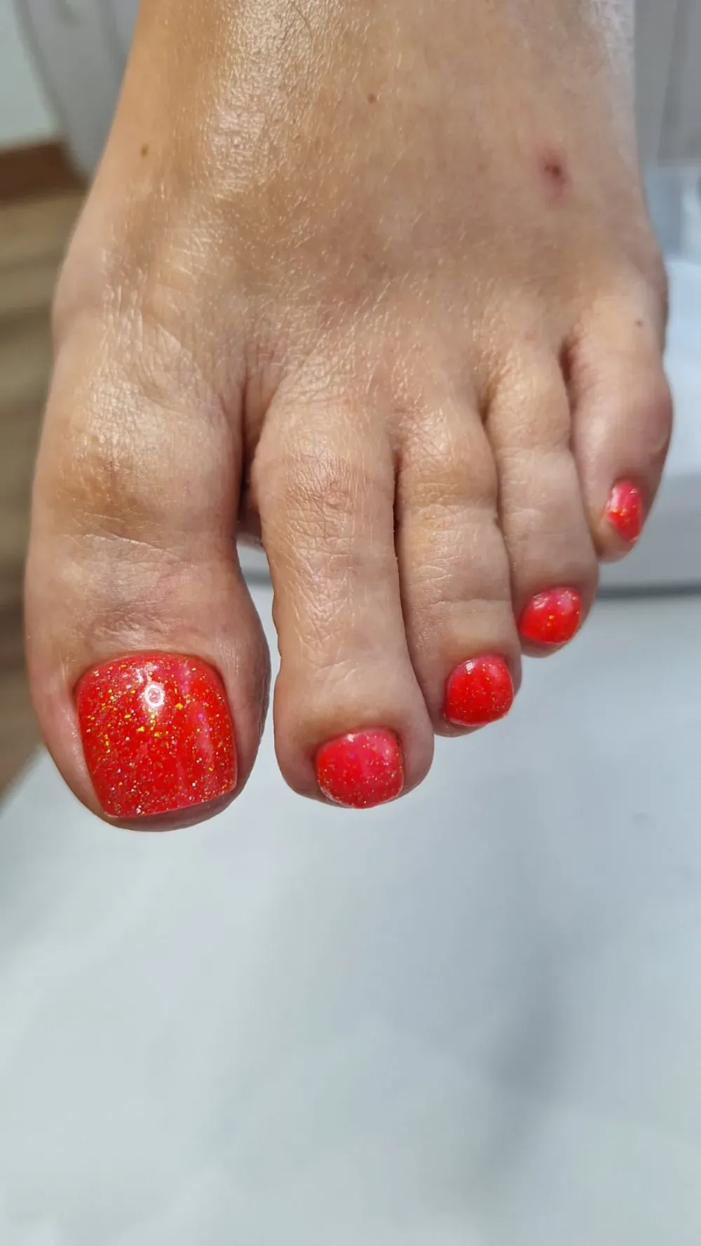 Pie con esmalte de uñas rojo, incluyendo esmalte brillante en el dedo gordo.