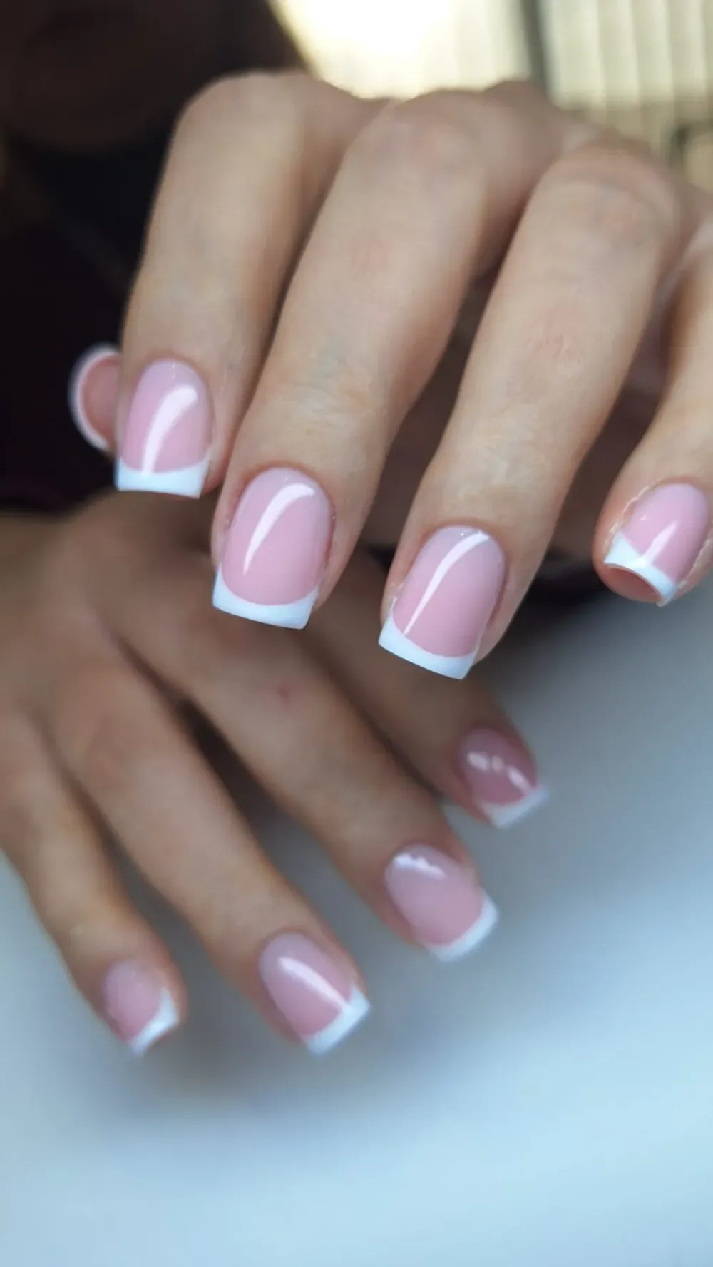 Manos con manicura francesa cuadrada, uñas rosa claro con puntas blancas.