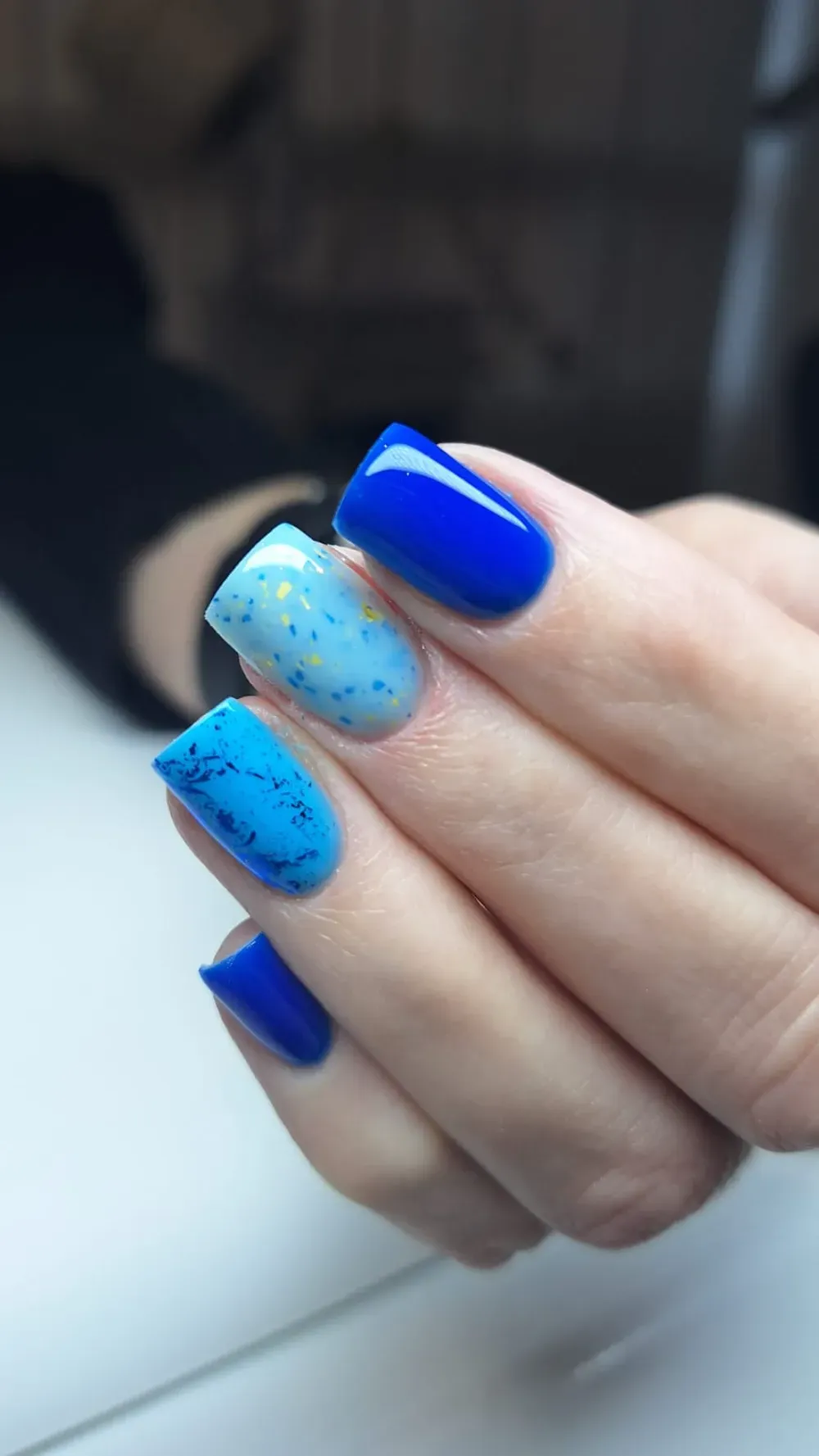 Mano con uñas cuidadas en forma de cuadrados de color azul y celeste.
