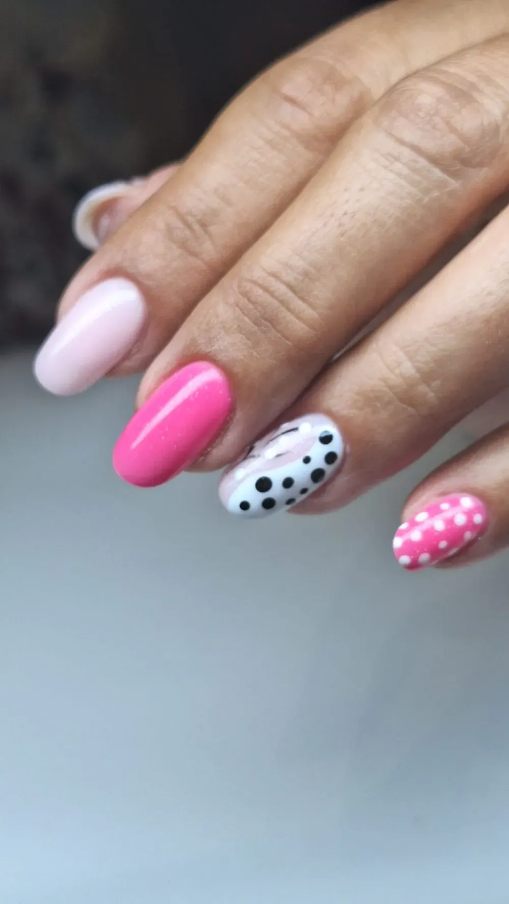 Mano con uñas decoradas en tonos rosas y lunares; uñas de forma ovalada.